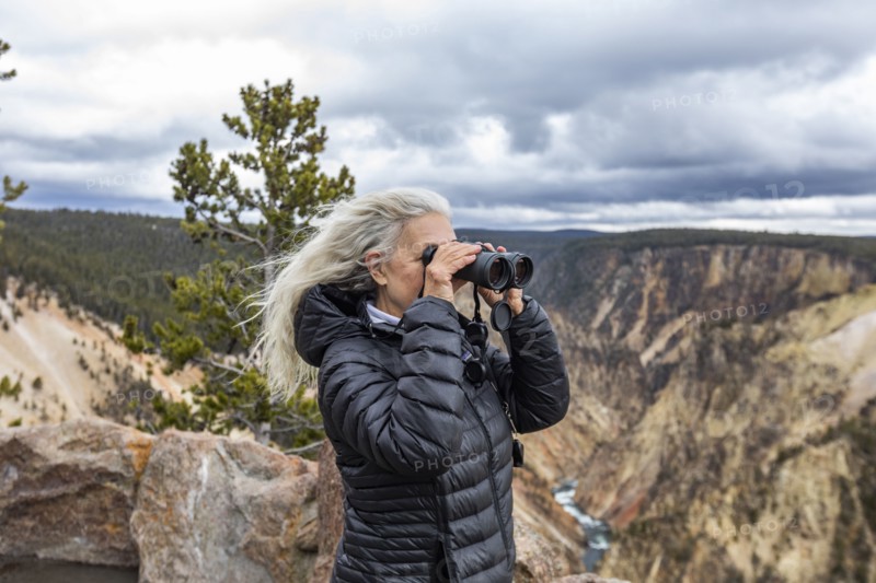 Senior woman looking through binoculars while standing above Grand Canyon in Yellowstone National Park