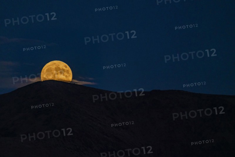 Full moon rising over mountains at night