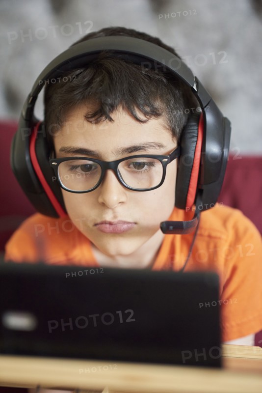 Boy (8-9) gaming on tablet while sitting in bed during weekend