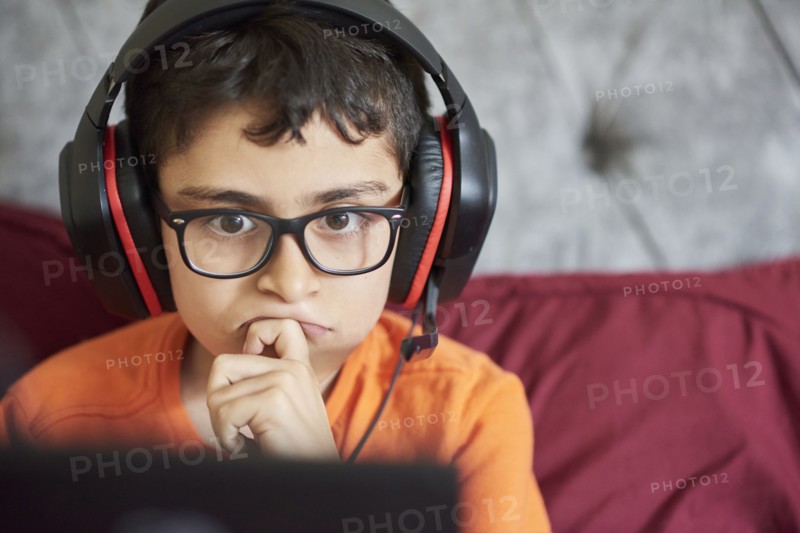 Boy (8-9) gaming on tablet while sitting in bed during weekend