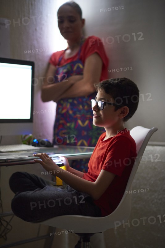 Mother watching son (8-9) during e-learning at home due to Covid-19 lockdown