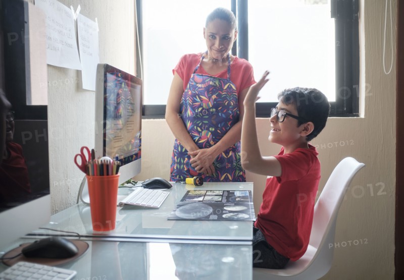 Mother watching son (8-9) during e-learning at home due to Covid-19 lockdown