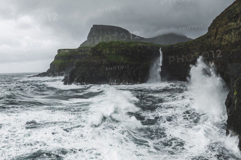 Coastline with Mulafossur Waterfall falling into Atlantic Ocean in stormy day