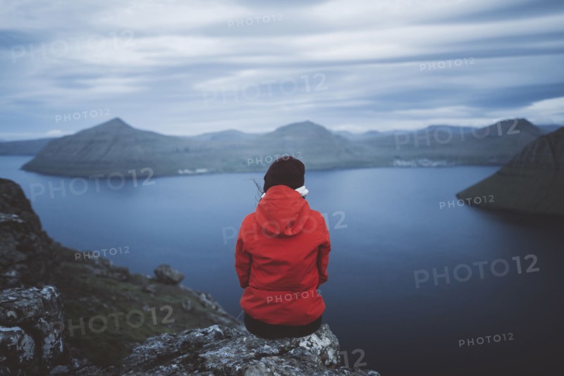 Woman sitting on edge of cliff over sea and looking at view