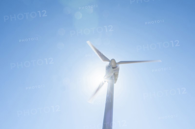 Low angle view of wind turbine against blue sky and sun