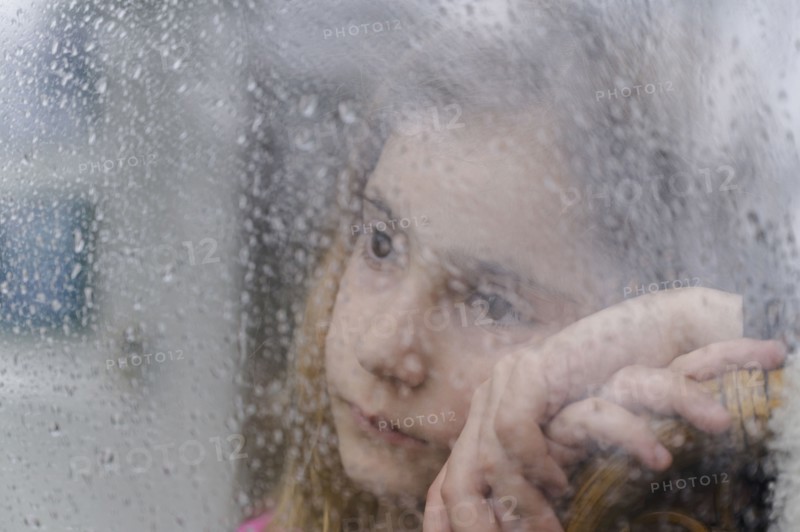 Close-up of girl (8-9) looking through window on rainy day