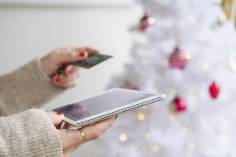 Hands holding tablet and credit card next to Christmas tree