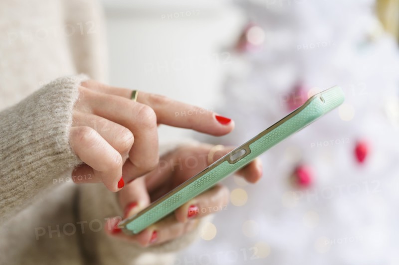 Hands holding smartphone next to Christmas tree