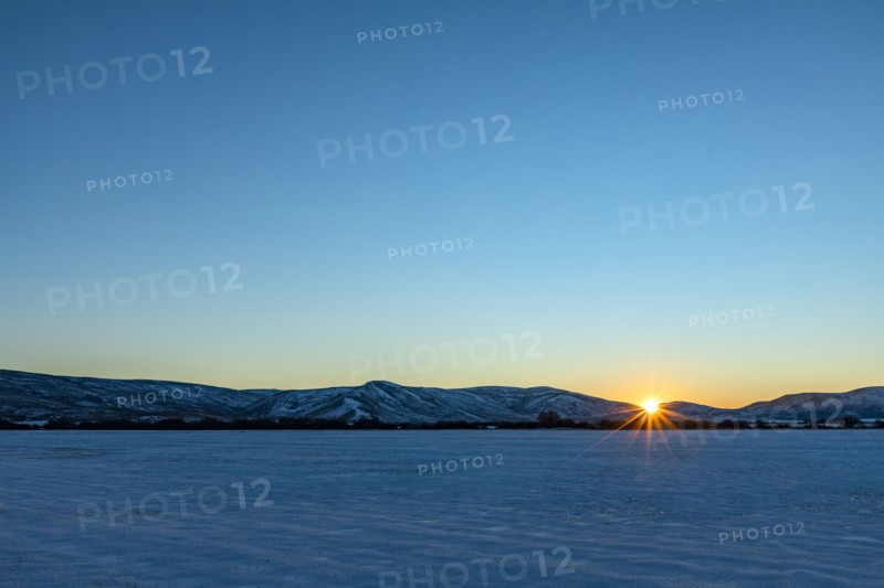 Sun setting over snowy field and mountains