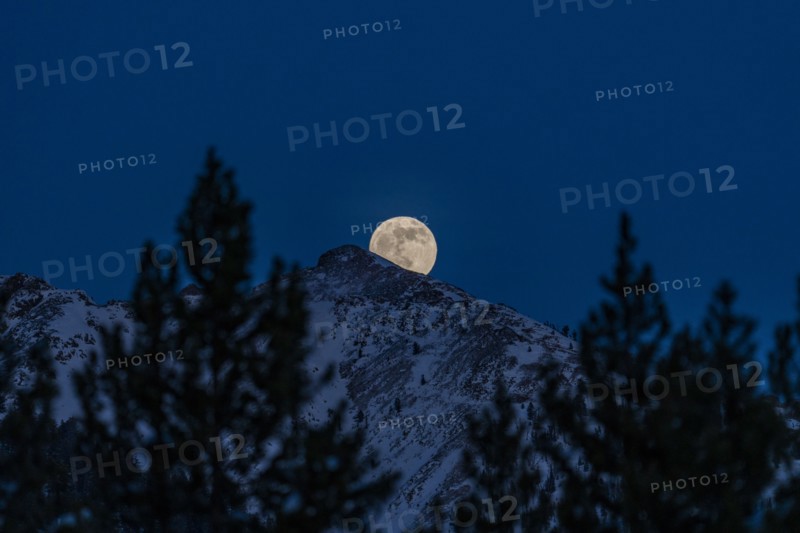 Full moon rising over Boulder Mountains in winter night