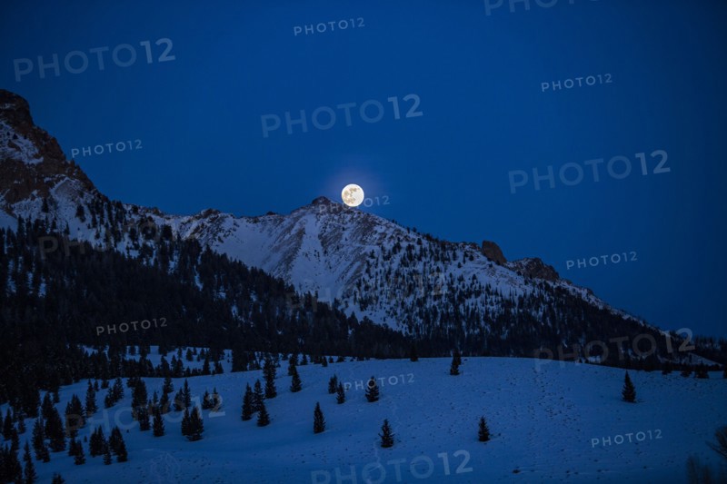 Full moon rising over Boulder Mountains in winter night