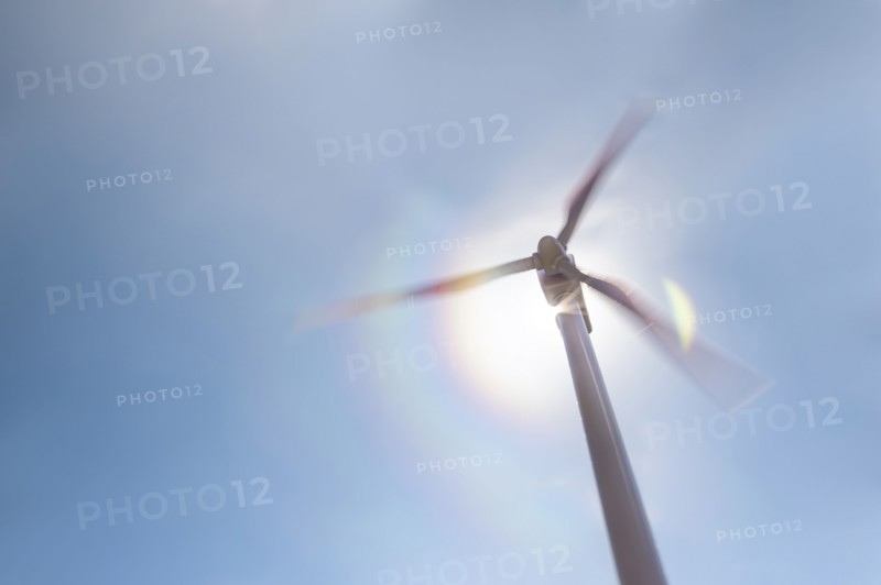 Low angle view of wind turbine against blue sky and sun