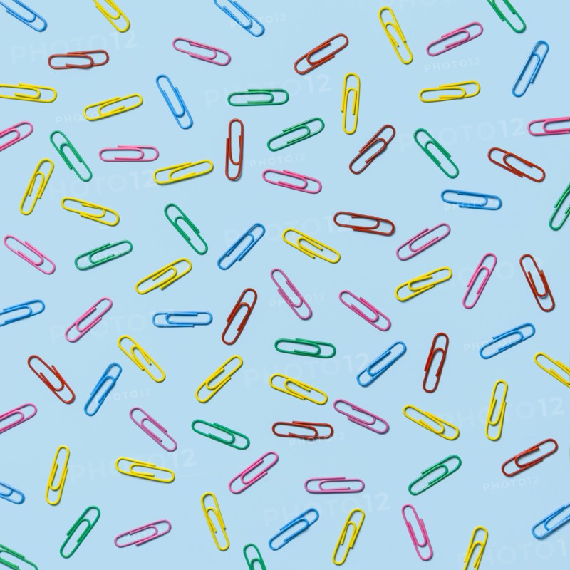 Multi colored paper clips scattered against blue background