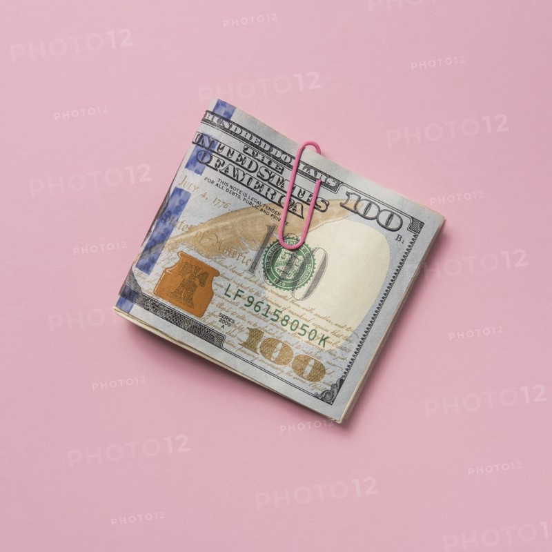 Folded one hundred dollar bill with paper clip on pink background