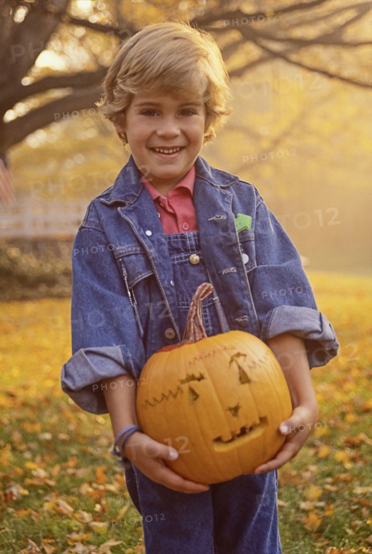 Portrait of smiling boy (4-5) holding carved Halloween pumpkin in field