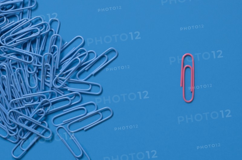 One pink paper clip and pile of blue paper clips