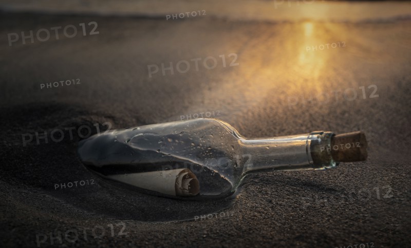 Glass bottle with message inside on beach at sunset