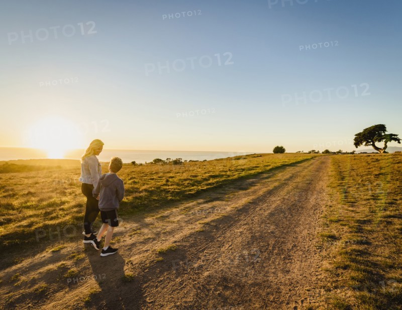 Rear view of mother and son walking in landscape at sunset