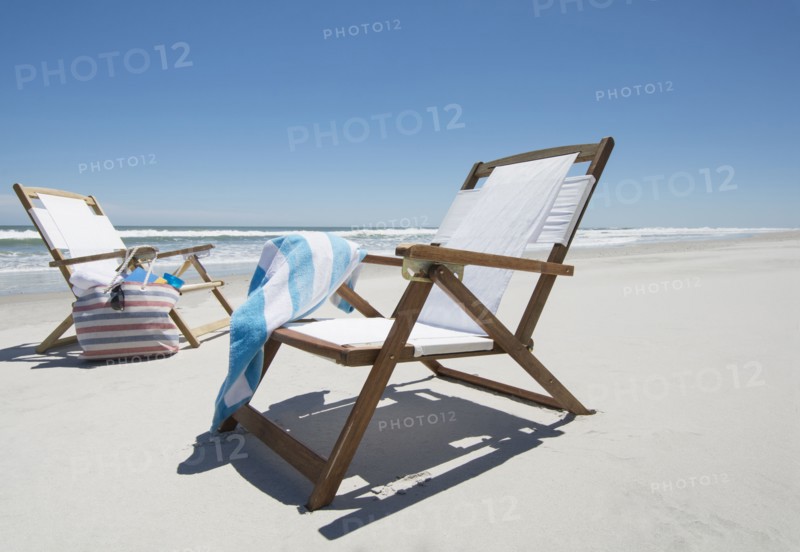 Empty beach chairs with bag and towel on beach