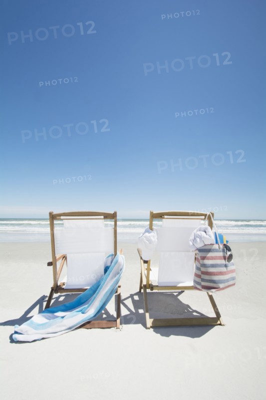 Empty beach chairs with bag and towel on beach