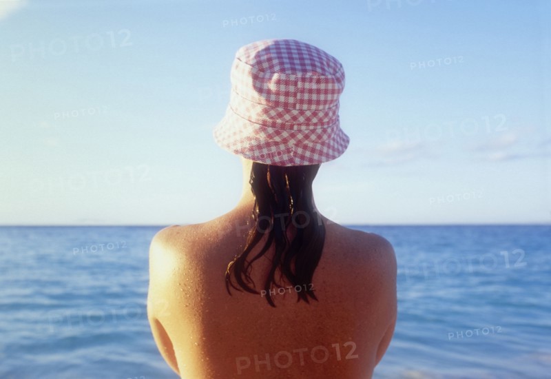 Rear view of woman in sunhat looking at sea