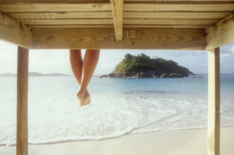Legs of woman sitting on wooden pier above sea