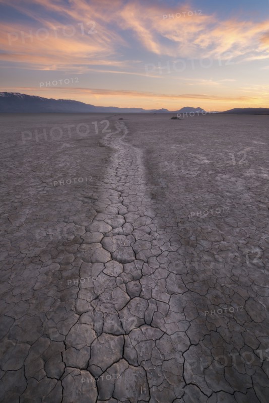 Path at cracked desert area at sunset