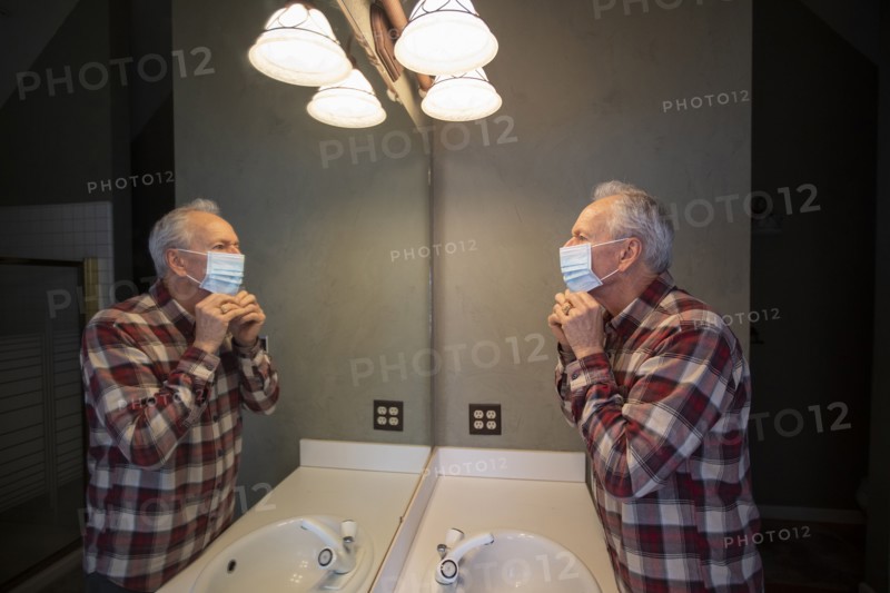 Senior man adjusting protective mask looking in bathroom mirror