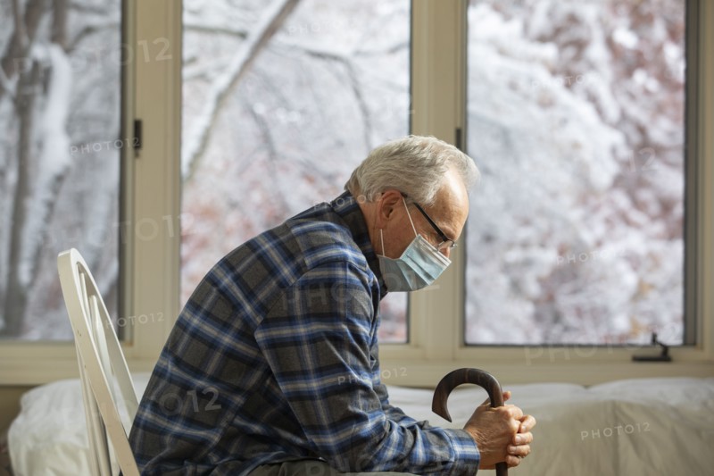Senior man wearing protective mask sitting near window