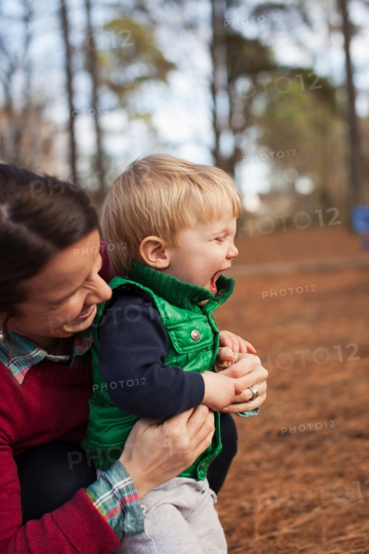 Laughing mother tickling son in park