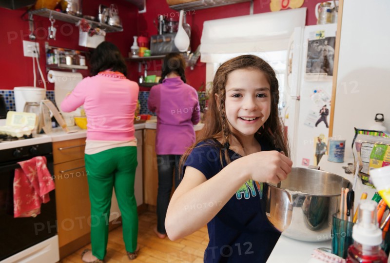 Girl in kitchen with mother and sister in background