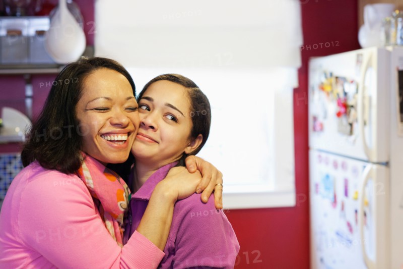 Portrait of mother hugging daughter in kitchen