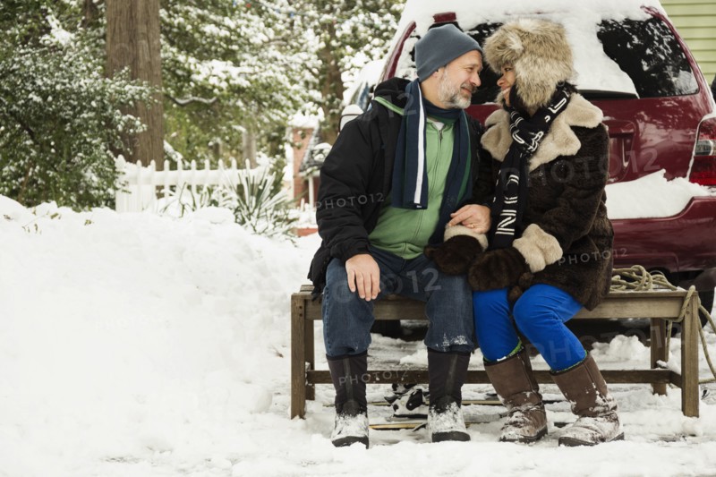 Mature couple sitting on toboggan in snow