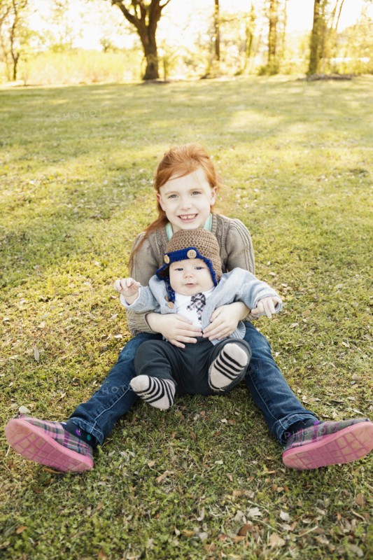 Portrait of girl and baby brother on grass in park
