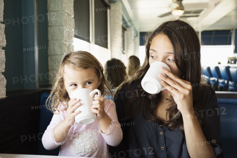 Mother and toddler drinking mugs of coffee in diner