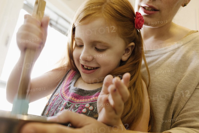 Girl mixing ingredients in bowl with mother in kitchen
