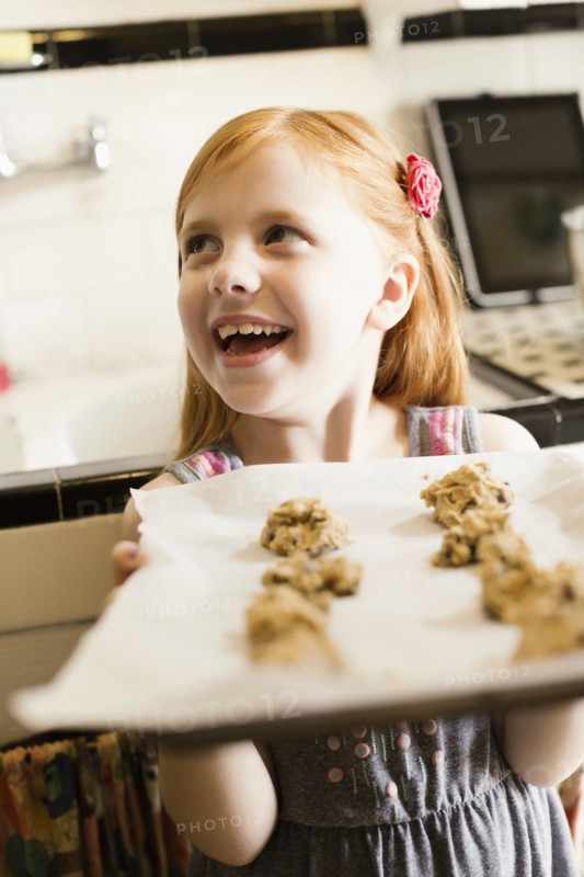 Girl holding up tray of biscuits in kitchen