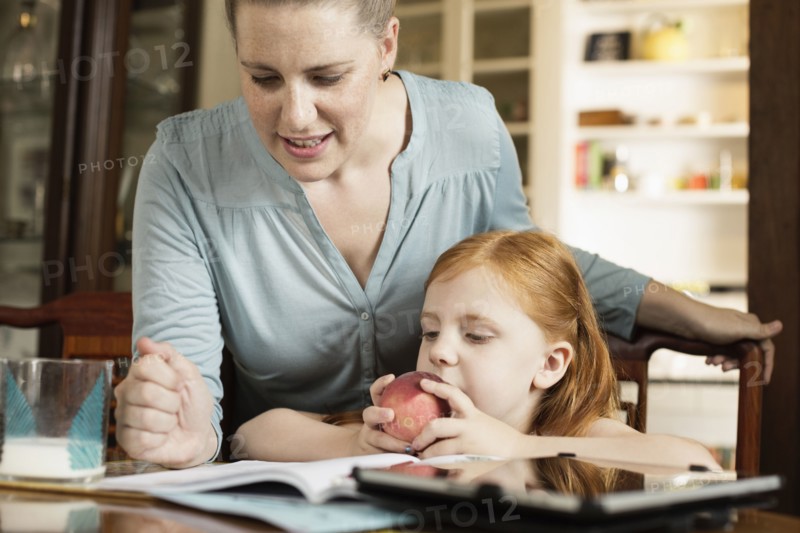 Mid adult mother helping daughter with homework at dining room table