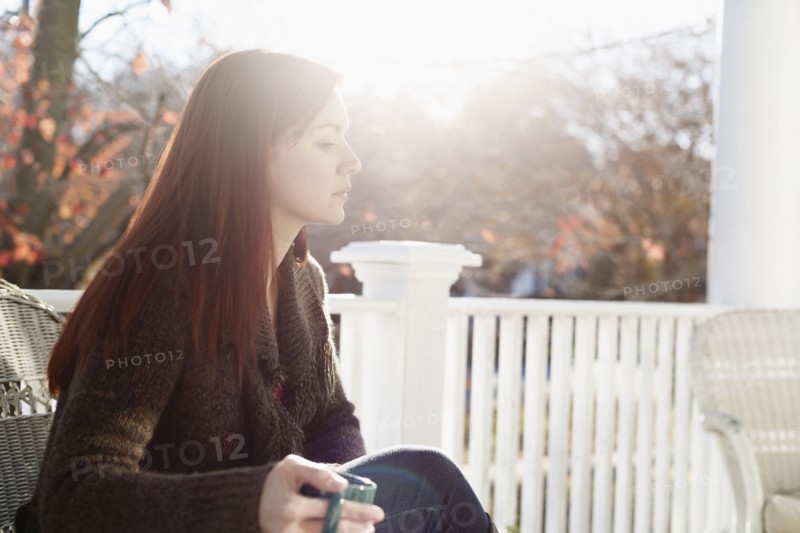 Young woman drinking coffee with eyes closed in porch