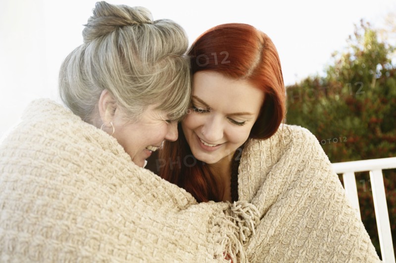 Senior woman and adult daughter face to face wrapped in a blanket on porch