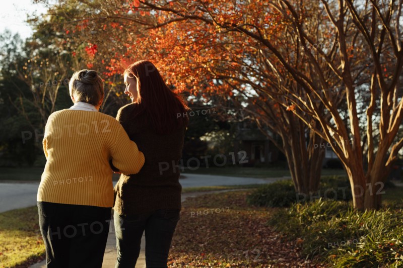 Rear view of senior woman and adult daughter strolling in suburban park