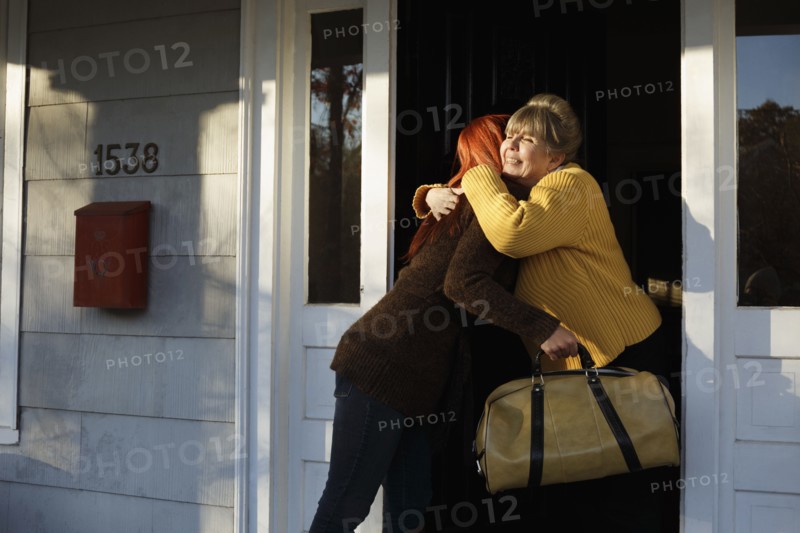 Senior woman and adult daughter hugging at front door