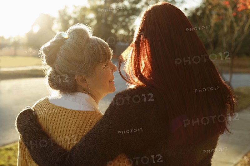 Rear view of senior woman and adult daughter strolling in park