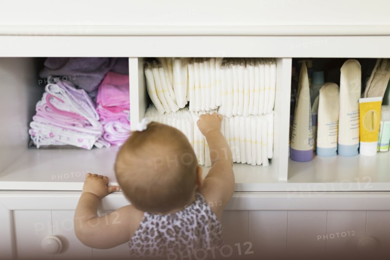 Rear view of baby girl reaching for diaper in cupboard