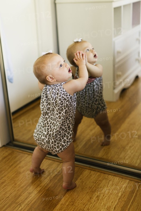 Baby girl leaning against mirrored wardrobe in bedroom