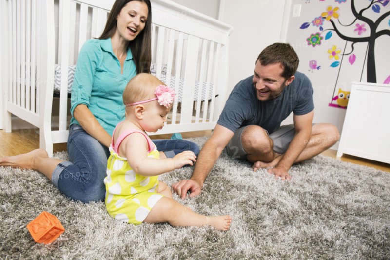 Mid adult couple playing with baby daughter on nursery rug