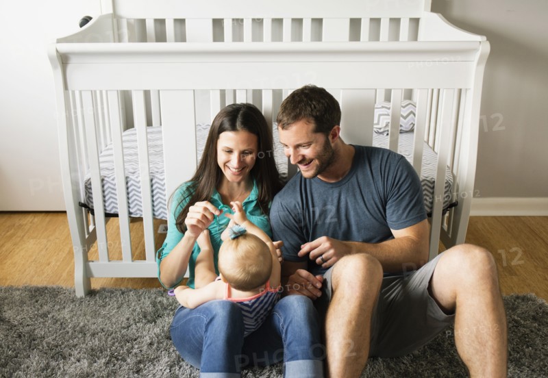 Mid adult couple playing with baby daughters fingers on lap
