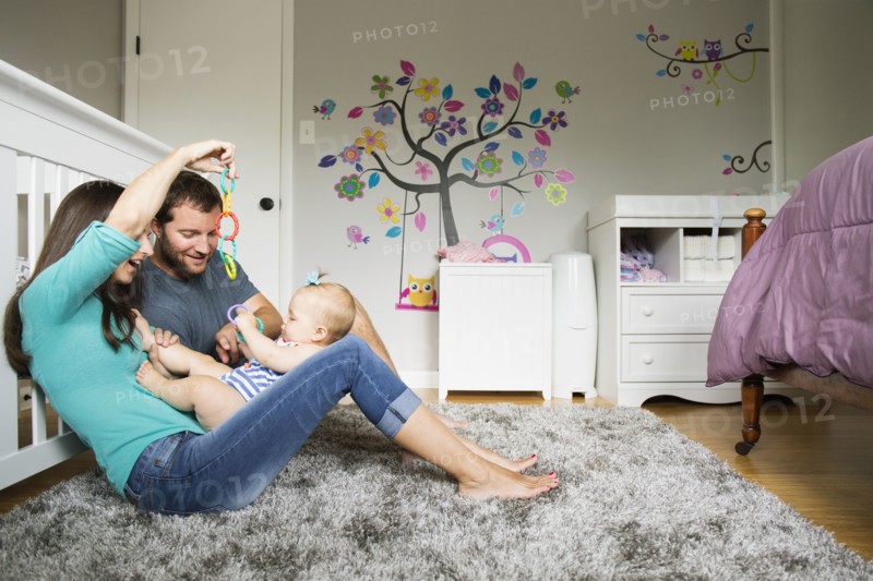 Mid adult couple playing with baby toy and baby daughter on lap
