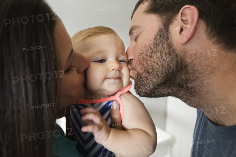 Close up of mid adult couple kissing baby daughter on each cheek