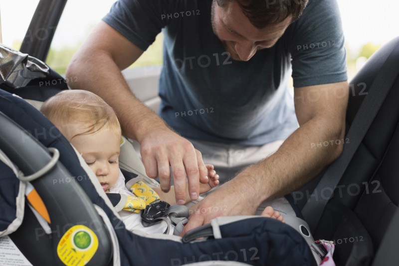 Mid adult man fastening safety belt on baby daughters car seat